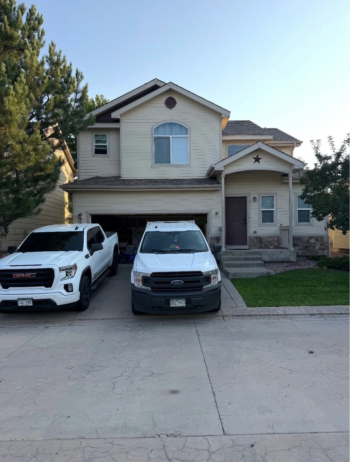 Cream two-story house before Chess Remodels exterior repaint, with Chess work trucks in driveway